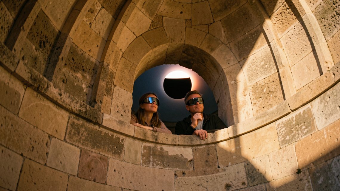 Une femme et un homme portant des lunettes de protection observent une éclipse solaire depuis une coupole historique en pierre, éclairée par la lumière chaleureuse de la fin de journée.
