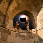 Une femme et un homme portant des lunettes de protection observent une éclipse solaire depuis une coupole historique en pierre, éclairée par la lumière chaleureuse de la fin de journée.