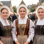 Portrait documentaire de trois jeunes femmes bretonnes en costumes traditionnels, coiffes en dentelle et vêtements brodés, lors d’un festival à Quimper.