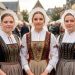 Portrait documentaire de trois jeunes femmes bretonnes en costumes traditionnels, coiffes en dentelle et vêtements brodés, lors d’un festival à Quimper.