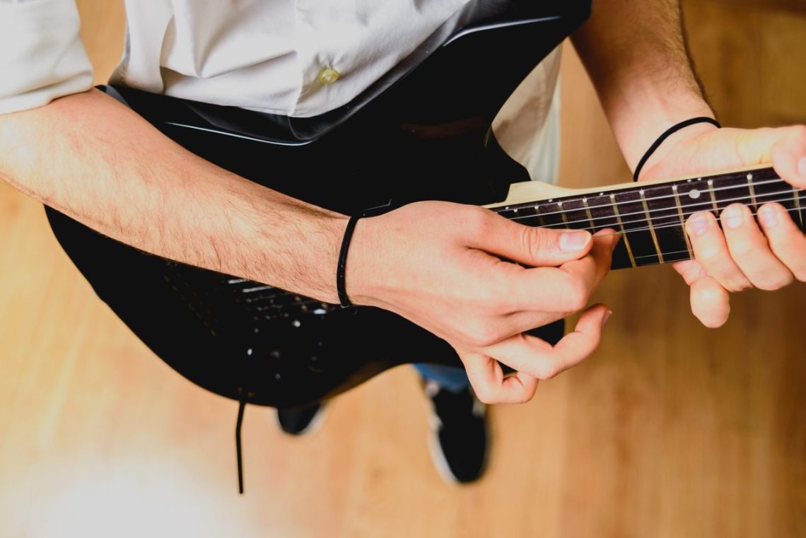 Guitariste jouant un accord de si majeur à la guitare avec un barré sur le manche.